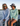 Two people sitting on a dock by a body of water, wearing sunglasses and casual clothing.