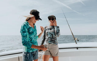 Two women wearing stylish women's fishing outfits on a boat with ocean in the background