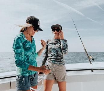 Two women wearing stylish women's fishing outfits on a boat with ocean in the background