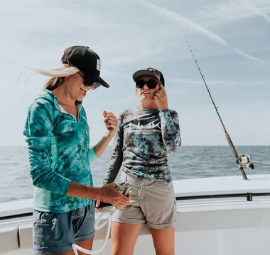 Two women wearing stylish women's fishing outfits on a boat with ocean in the background