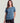 Woman wearing a blue-grey short-sleeve tee with a circular chest pocket graphic, paired with black shorts.