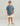 Child wearing slate blue short-sleeve tee with small embroidered logo, cream shorts, and tan boat shoes.