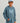 Child wearing slate blue Huk hoodie with large logo print, front kangaroo pocket, and drawstring hood.