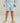 Light blue swim shorts with dark shark and circle pattern, white drawstring waist, worn with gray long-sleeve shirt.