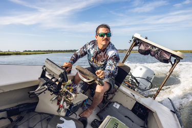 Man on a boat wearing Huk performance gear with a clear sky and water background